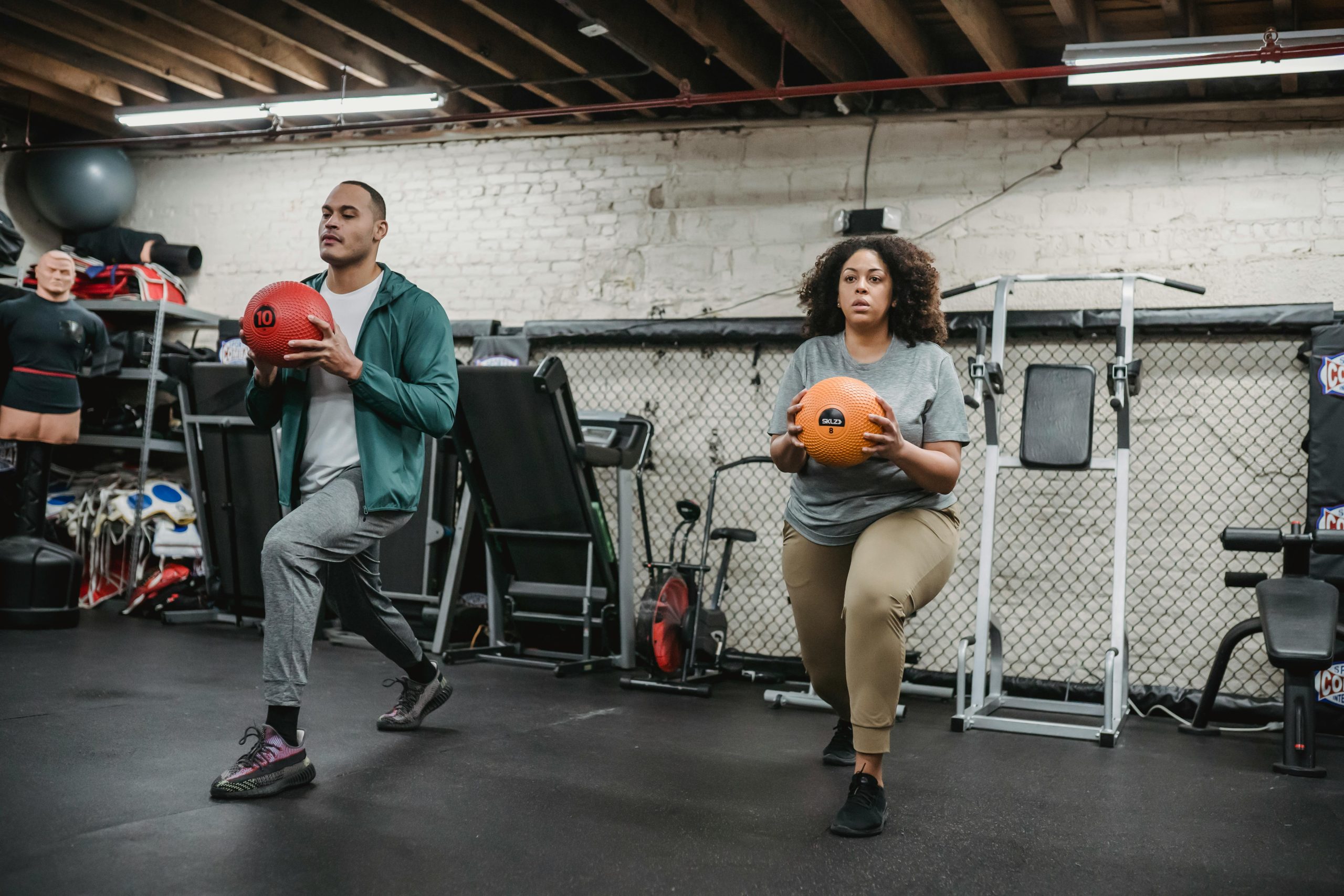 Two people doing lunges with medicine balls in a gym, showcasing focus and fitness.